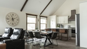 Una cocina moderna con armarios blancos, un refrigerador de acero inoxidable y un comedor con sillas de cuero y una mesa de madera.
