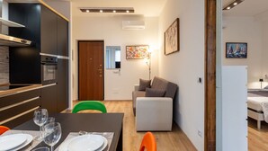 A modern kitchen with built-in appliances, a dining area with a table set for four, and a living area with a sofa and a painting. - Cosy apartment for 3 guests with A/C, WIFI, TV and balcony (Milan)