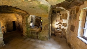 Una habitación subterránea con paredes de piedra, suelo de baldosas y un estante de madera con botellas.