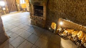 Una habitación de paredes de piedra con chimenea, suelo de baldosas y una pila de leña.