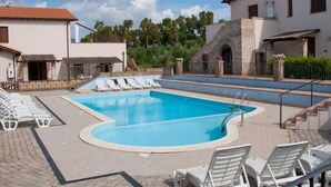 Una piscina con sillas de descanso, un edificio de piedra y un cielo despejado.