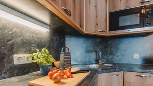 Una cocina moderna con armarios de madera, microondas integrado, un lavamanos y una tabla de cortar con tomates y albahaca.