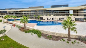 Et moderne hotel med central pool, flere balkoner og et velholdt udendørs område med palmer.