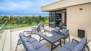 En moderne udendørs terrasse med et bord, stole, en sofa og en glasdør, der fører ind i et rum.