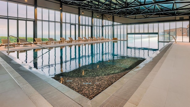 En indendørs swimmingpool med krystalklart udsyn til det omkringliggende landskab, store vinduer og moderne arkitektur.