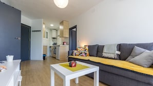 Un salon moderne avec un canapé, une petite table blanche et une cuisine en arrière-plan.