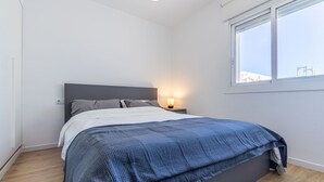 Une chambre à coucher avec un lit, une table de chevet, une lampe et une fenêtre.