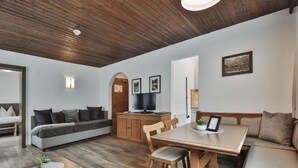 A modern living room with a wooden ceiling, a sofa, a dining table with chairs, and a TV. - Lovely apartment for 5 guests with WIFI, TV, terrace and pets allowed (Ischgl)