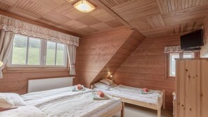 Habitació d'un xalet acollidor amb dos llits superposats de fusta, una finestra amb cortines, un radiador i un televisor fixat a la paret.
