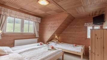 Une chambre confortable de style cabane, avec deux lits superposés en bois, une fenêtre avec des rideaux, un radiateur et un téléviseur fixé au mur.