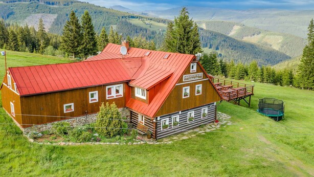Una cabana de fusta amb teulada vermella, envoltada per un paisatge verd i exuberant, amb muntanyes al fons.