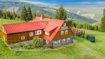Une cabane en bois avec un toit rouge, entourée d’un paysage verdoyant et luxuriant, avec des montagnes en arrière-plan.