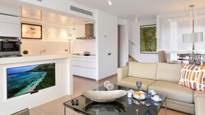 A modern living room with a flat-screen TV, a sofa, a coffee table, and a dining area with a small table and chairs.