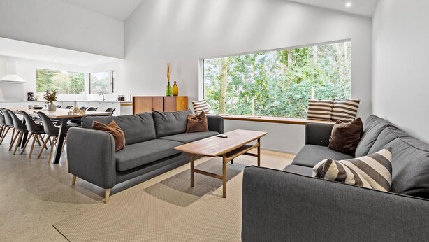 A modern living room with a grey sofa, a wooden coffee table, and a dining area with a white table and chairs.