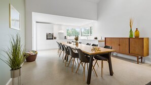 A modern kitchen with white cabinetry, a large dining table, and a wooden cabinet with decorative bottles.