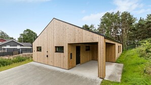 A modern wooden building with a sloped roof, a concrete driveway, and a grassy area with trees in the background.