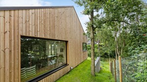 A modern wooden building with large windows and a grassy yard.