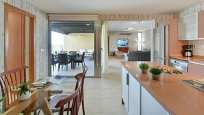 Une cuisine moderne dotée d’un îlot central, un coin repas avec des chaises et une table, et un espace de vie avec un canapé et une télévision.