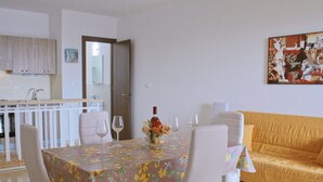 Een eetgedeelte met een tafel voor vier personen, witte stoelen en een tafelkleed met bloemenmotief.