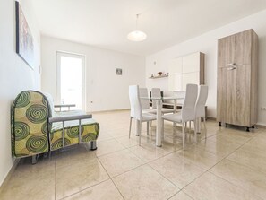 A modern dining area with a glass table and white chairs, a wooden wardrobe, and a patterned bench.