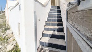 Una escalera conduce a la entrada de un edificio con fachada blanca y barandilla de madera.