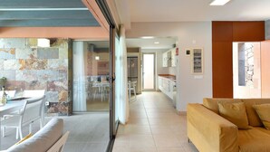 A modern living room with a sofa, a dining area with a table and chairs, and a kitchen area with cabinets and a refrigerator.