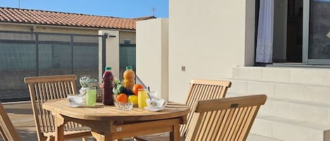 Un patio al aire libre con una mesa redonda de madera y sillas, rodeado por un muro blanco y una ventana.