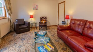 A living room with a brown leather sofa, a red leather sofa, a brown armchair, and a glass coffee table with Scrabble tiles and books. - Lovely apartment for 4 people with TV and terrace (Inverness)