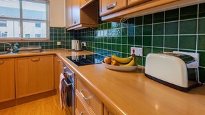 A kitchen with wooden cabinets, a black induction cooktop, a toaster, and a bowl of fruit on the counter. - Lovely apartment for 4 people with TV and terrace (Inverness)