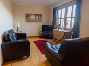 Una sala de estar con dos sofás de cuero negro, una mesa de centro de madera, un televisor y un cuadro en la pared.