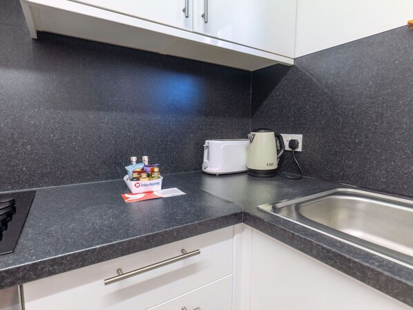 A kitchen with a black countertop, white cabinets, a kettle, and a small container with toiletries.