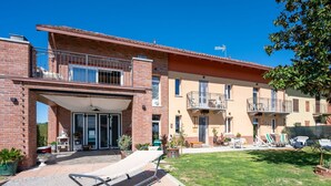 A two-story brick building with a covered entrance, outdoor seating, and a small lawn. - Stunning  villa for 10 people with A/C, private pool, WIFI and patio (San Damiano D'asti)