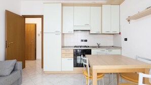 A compact kitchen with white cabinets, a wooden dining table, and a grey sofa. - Cosy apartment for 4 guests with A/C, WIFI, TV, balcony and pets allowed (Diano Marina)