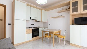 A modern kitchen with white cabinets, a dining table with chairs, and a TV on a shelf. - Cosy apartment for 4 guests with A/C, WIFI, TV, balcony and pets allowed (Diano Marina)