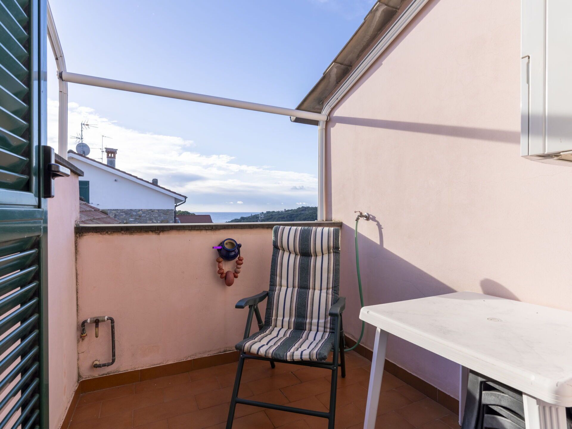 Un balcón con una silla a rayas, una mesita y vistas al mar.
