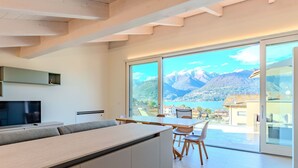 A modern kitchen with a built-in TV, a dining area with a table and chairs, and a large window offering a mountain view. - Stunning private villa for 10 guests with A/C, WIFI, private pool, terrace and pets allowed (Colico)