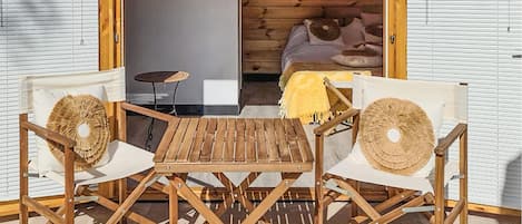 A wooden table and two chairs with woven seat cushions, set against a white wall with a wooden door frame.