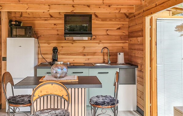 Cocina compacta con paredes de madera, microondas, estufa, lavamanos y comedor con dos sillas y una mesa.