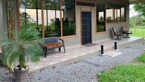 Een modern huis met grote glasramen, een overdekte veranda, een bank en een kleine tafel met stoelen.