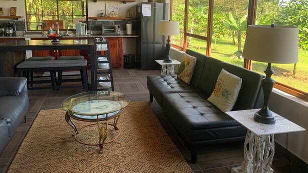 Een moderne woonkamer met een bank, een glazen salontafel en uitzicht op de keuken.