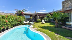 En swimmingpool med liggestole, en overdækket terrasse og en bygning i sten.