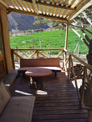 Une terrasse en bois avec un banc et une table, donnant sur un champ verdoyant et des montagnes.