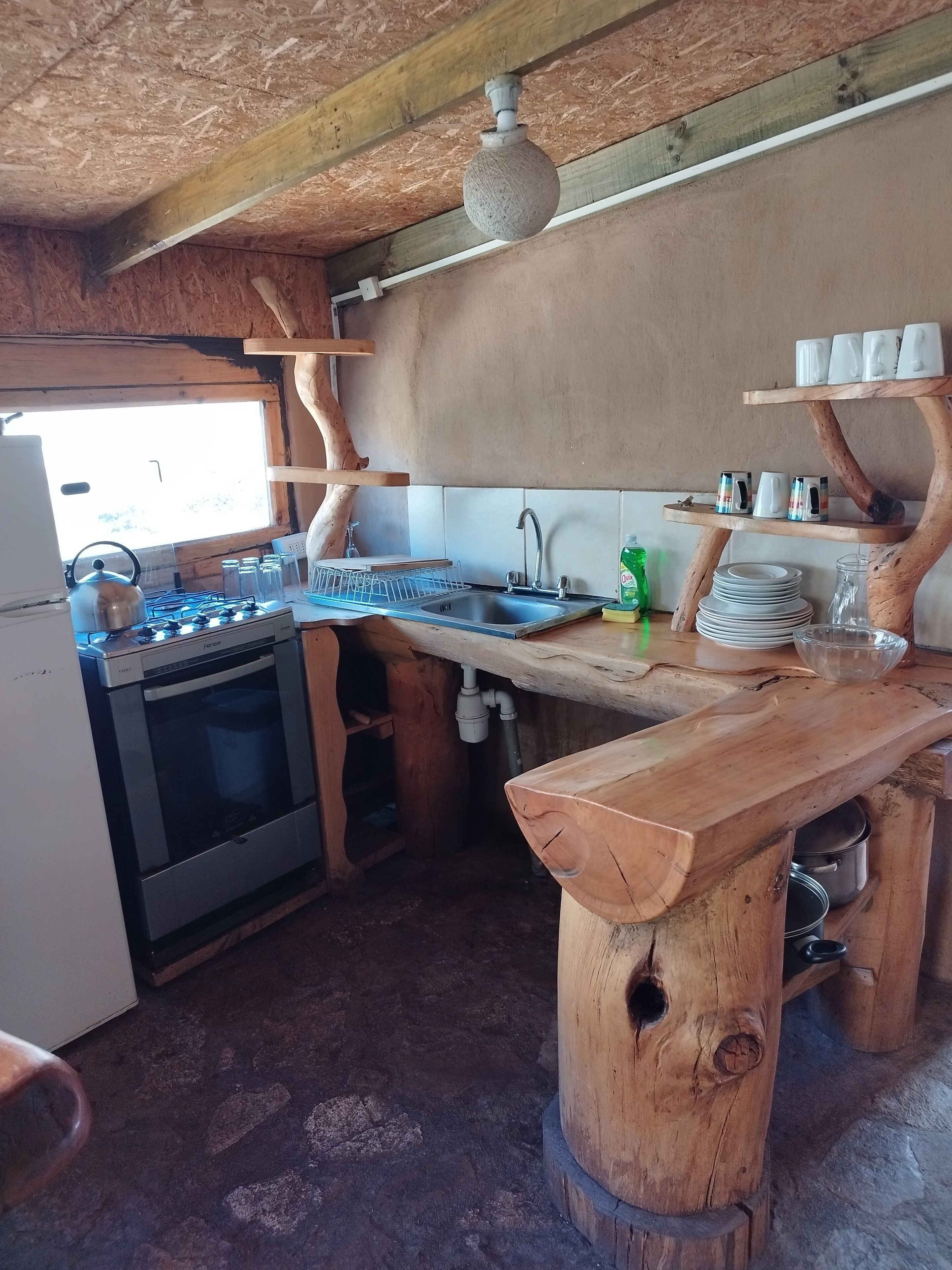 Une cuisine rustique avec un plan de travail en bois, une cuisinière à gaz, un évier et un luminaire suspendu.