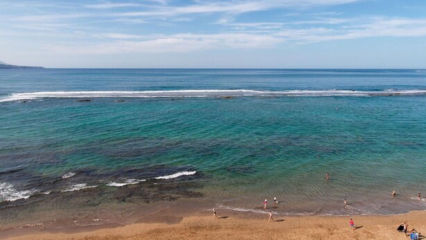 Una playa con agua turquesa cristalina, una orilla arenosa y una montaña distante.