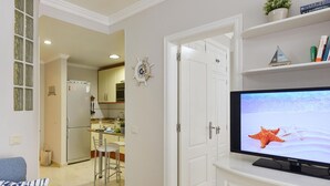 Una sala moderna con televisor de pantalla plana, comedor y cocina al fondo, además de un pasillo que conduce a otra habitación.
