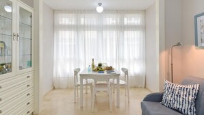 Un comedor con una mesa dispuesta para cuatro, un aparador con puertas de cristal y un sofá con un cojín estampado.