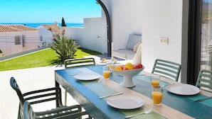 A dining table set with plates, cutlery, a bowl of fruit, and glasses of orange juice, overlooking a coastal view. - Stunning  villa for 6 guests with WIFI, pool, A/C, TV and terrace (Nerja)