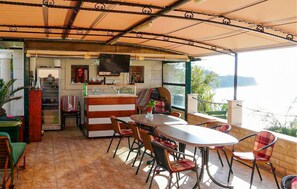 Een overdekt terras met eettafel en stoelen, een keuken met een televisie, en uitzicht op zee.