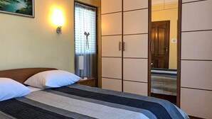 A hotel room with a bed, a nightstand, a lamp, a window with curtains, and a wardrobe. - Nice apartment in Privlaka (Privlaka)