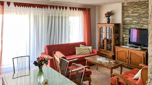 A living room with a red sofa, a glass coffee table, a wooden cabinet, and a television. - Nice apartment in Privlaka (Privlaka)